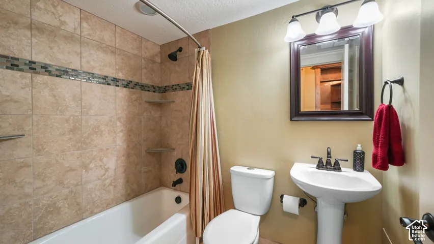 Bathroom featuring a tub-shower combination with tile surround and stone-look inlay, a pedestal sink with a dark-finish faucet, and a wall-mounted vanity mirror with integrated lighting