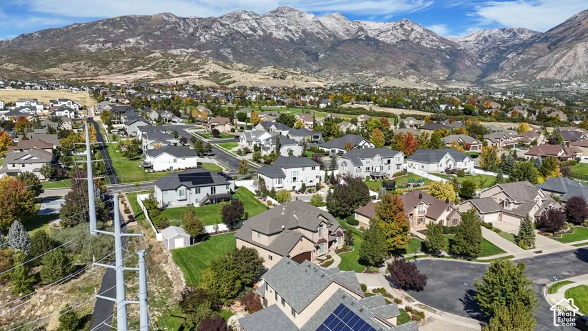 Aerial perspective of a residential neighborhood featuring mountain topography, mature trees, multi-level structures, and rooftop solar panel arrays