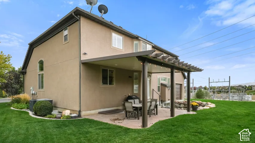 Stucco exterior featuring a covered patio, pergola, stone-edged landscaping, and manicured lawn