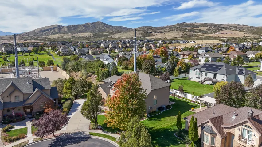 Aerial perspective featuring multi-story residential properties with asphalt shingle roofing, attached garages, and manicured lawns, set against a backdrop of mountain terrain
