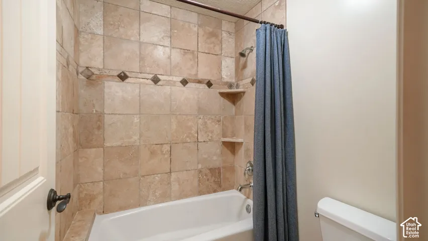 Full bathroom featuring a tub-shower combination with natural stone wall tiling, decorative stone accent detailing, integrated corner shelving, and a wall-mounted shower head