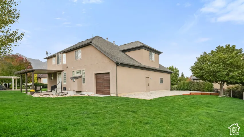 Exterior featuring a stucco facade, attached garage with wood-finish door, covered patio, and expansive lawn with mature landscaping