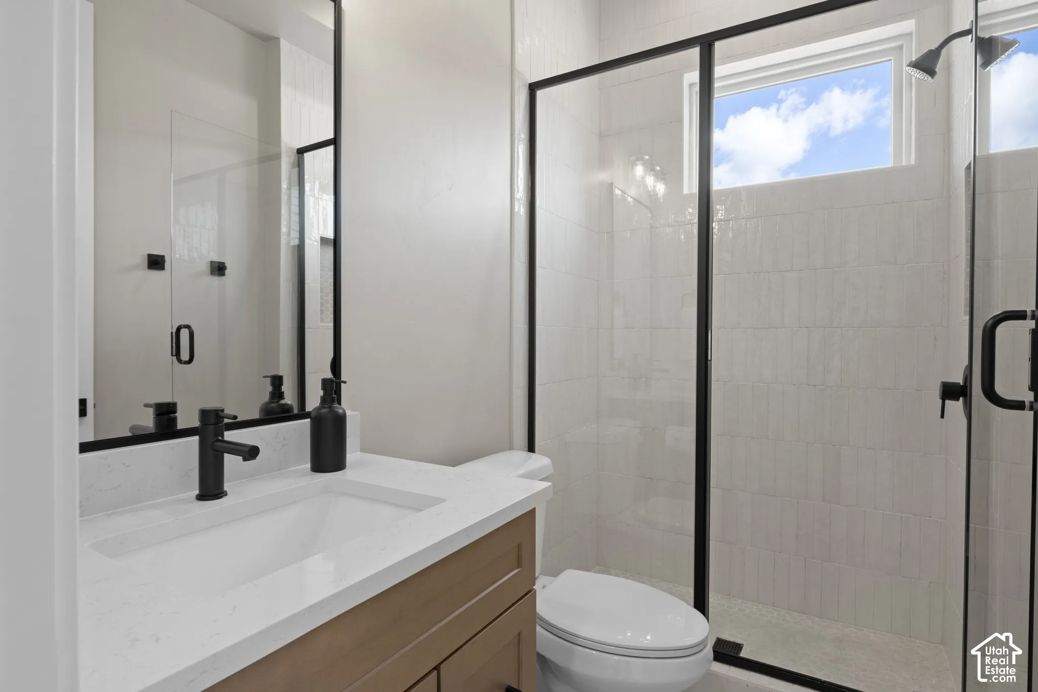 Bathroom featuring a wood-finish vanity with a stone countertop, an integrated sink with matte black hardware, a floor-to-ceiling framed mirror, and a walk-in shower with matte black-trimmed glass enclosure and wall tile