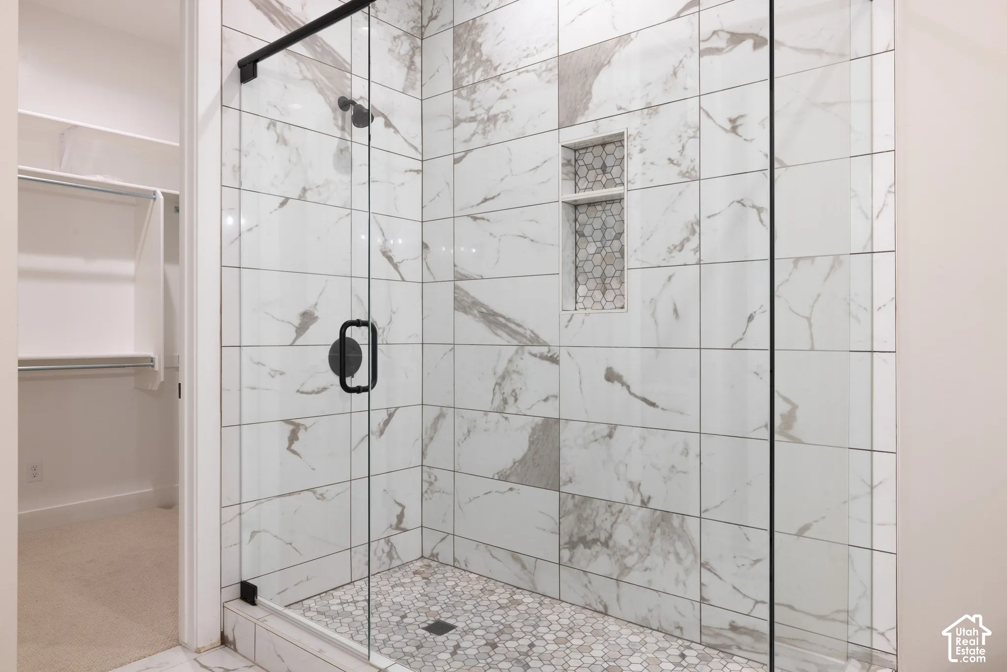 Walk-in shower featuring large-format stone-patterned tile, a recessed niche with mosaic detailing, a pebble-style tile floor, and a frameless glass enclosure with matte black hardware