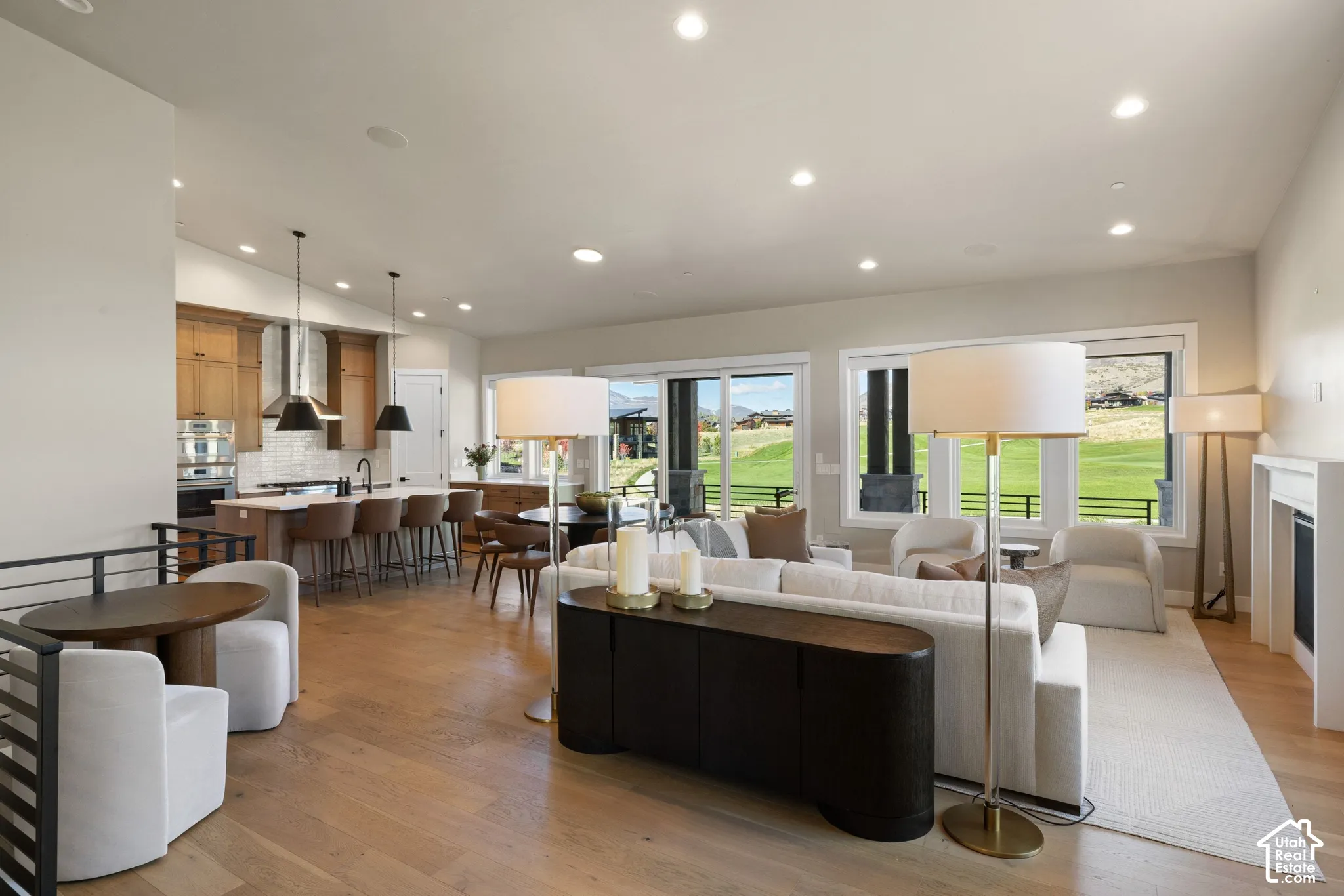 Open-concept living space featuring wood-finish flooring, recessed lighting, a kitchen with a center island and stone-finish countertops, and large sliding glass doors