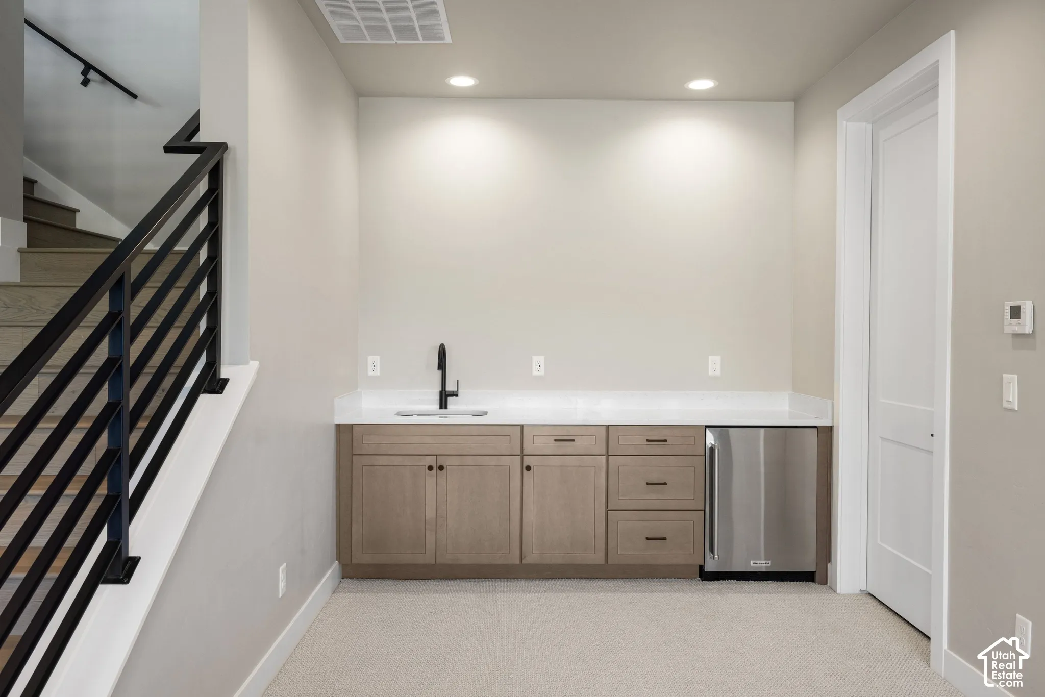 Built-in cabinetry featuring a stone-composite countertop, undermount sink with a matte black faucet, integrated stainless steel under-counter refrigerator, and staircase with metal horizontal railing