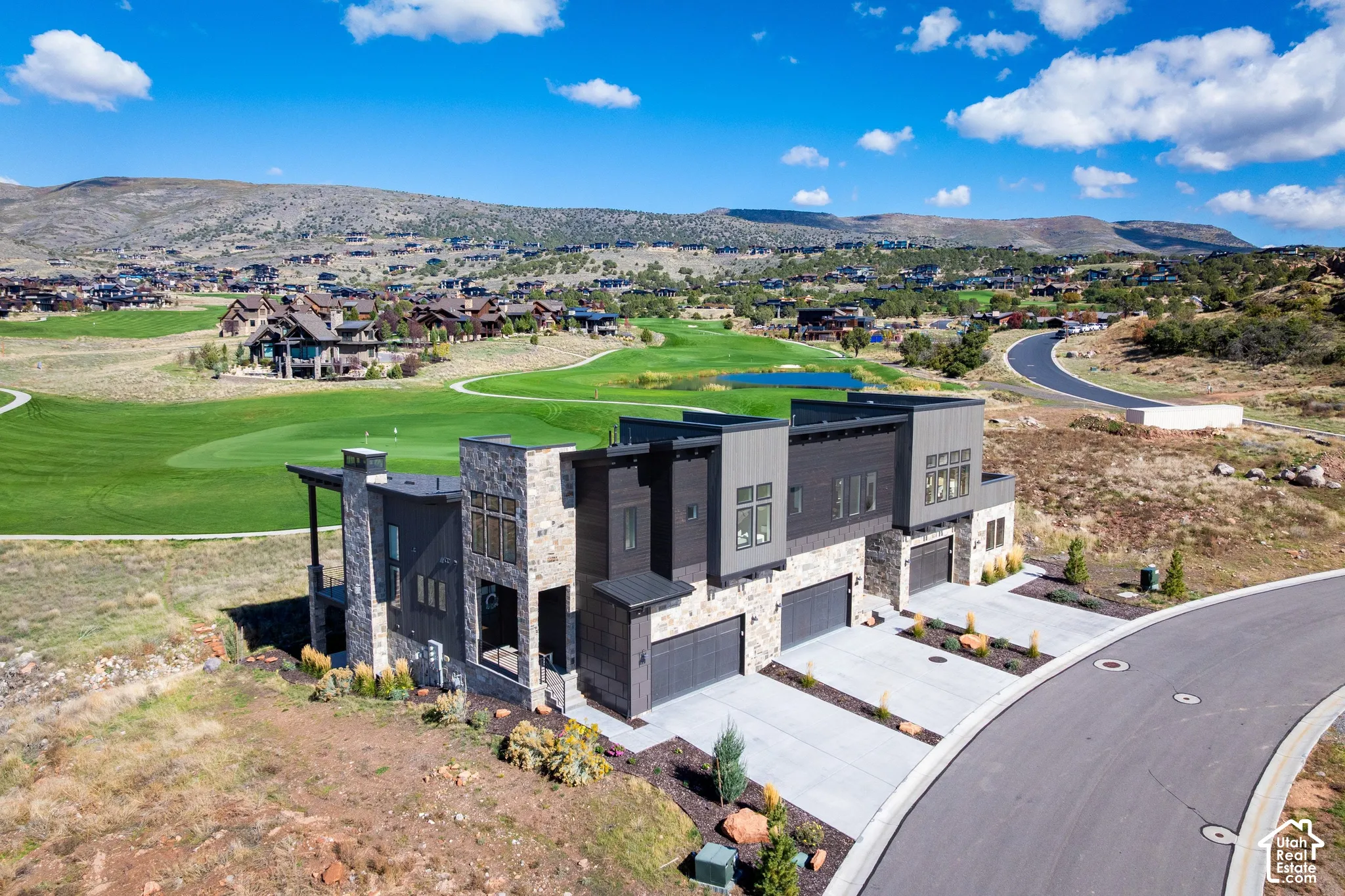 Modern multi-unit exterior featuring stacked stone masonry, vertical metal siding, concrete driveways, attached multi-car garages, and mountain terrain backdrop