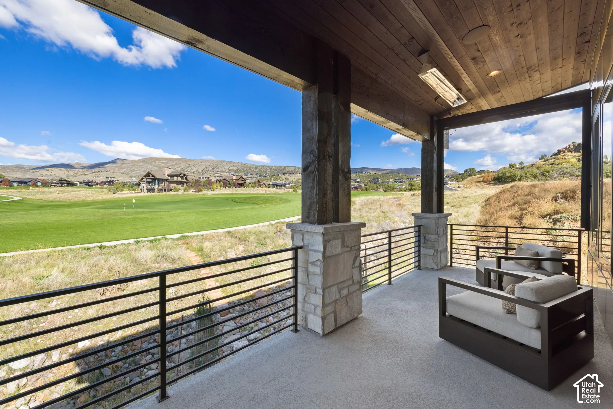 Covered patio featuring wood-paneled ceiling, stone-base support columns, metal railing, and overhead radiant heater