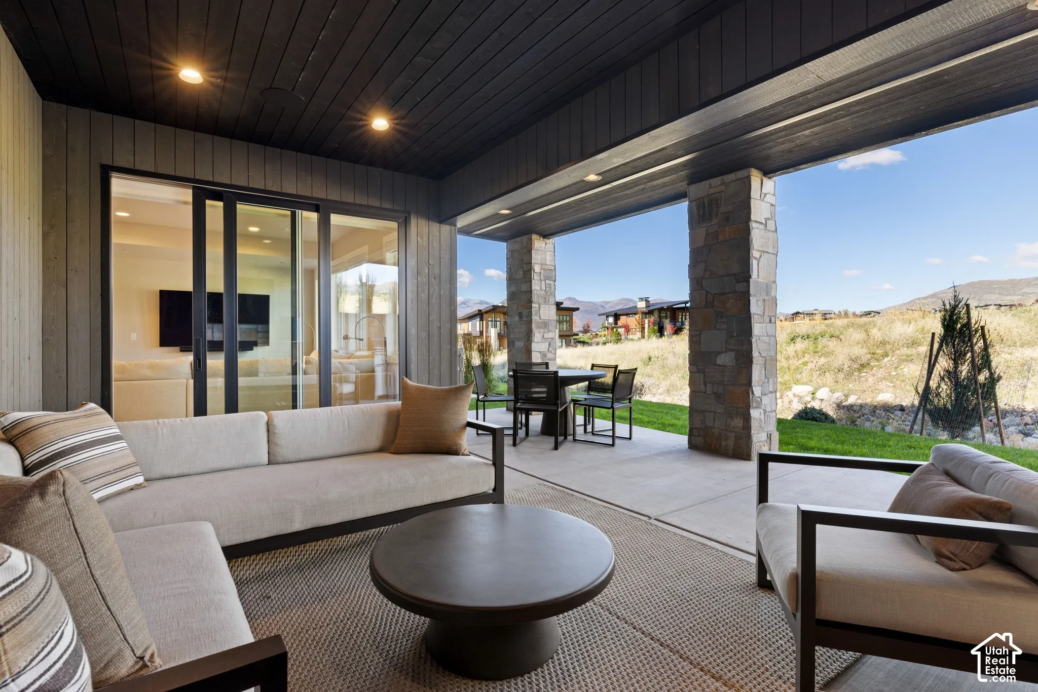 Covered patio featuring a wood-plank ceiling, natural stone support columns, recessed lighting, and large sliding glass doors