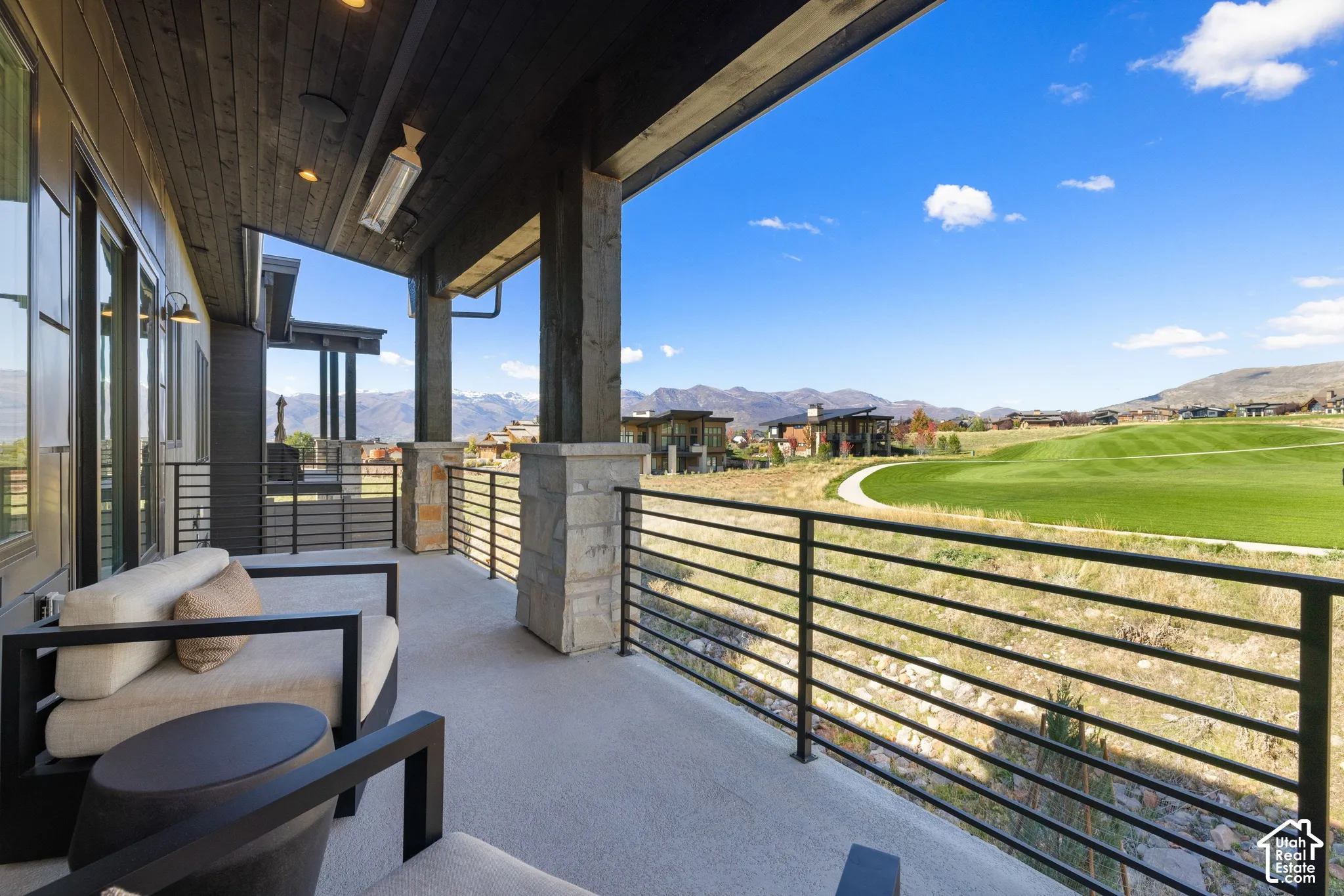 Covered balcony featuring a horizontal metal railing, stone-clad pillar supports, dark wood-finish ceiling, and mounted outdoor heating unit
