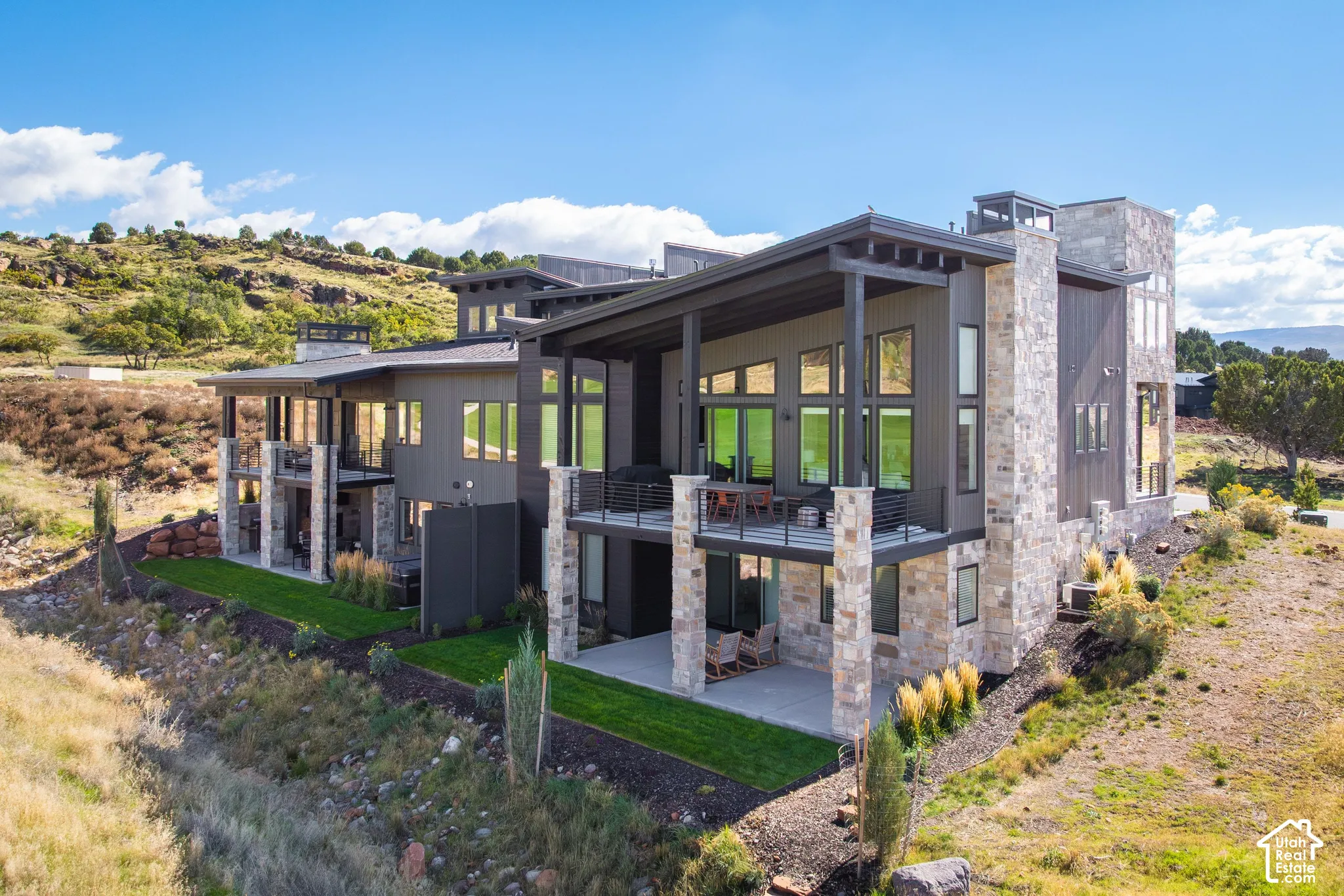 Contemporary multi-level exterior featuring stacked stone masonry, shed rooflines, metal-railed balconies, and a covered ground-level patio