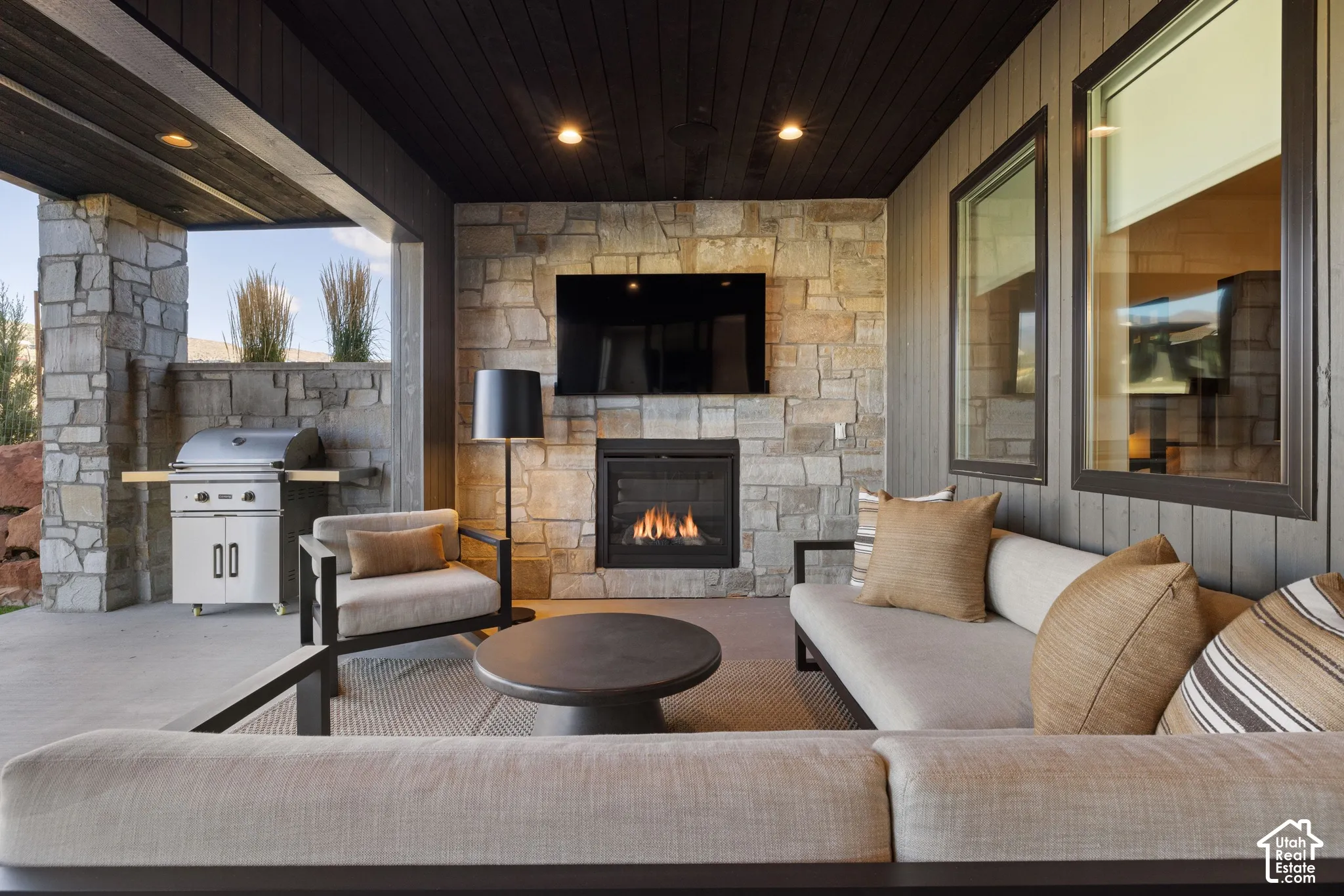 Covered patio featuring a stacked stone fireplace, built-in stainless steel outdoor grill, wood-plank ceiling, and recessed lighting