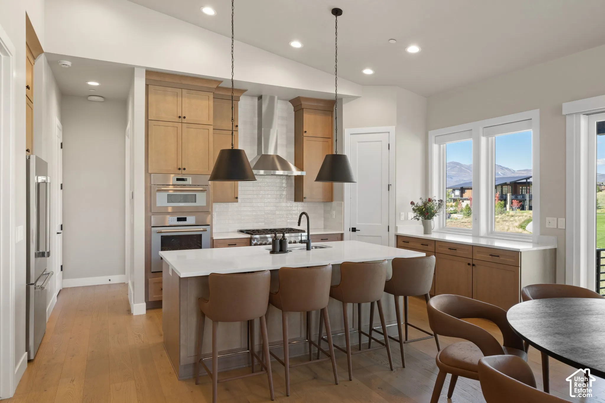 Kitchen featuring a quartz-topped central island, stainless steel built-in oven and microwave, stone-finish backsplash, wood-finish cabinetry, and matte black pendant lighting