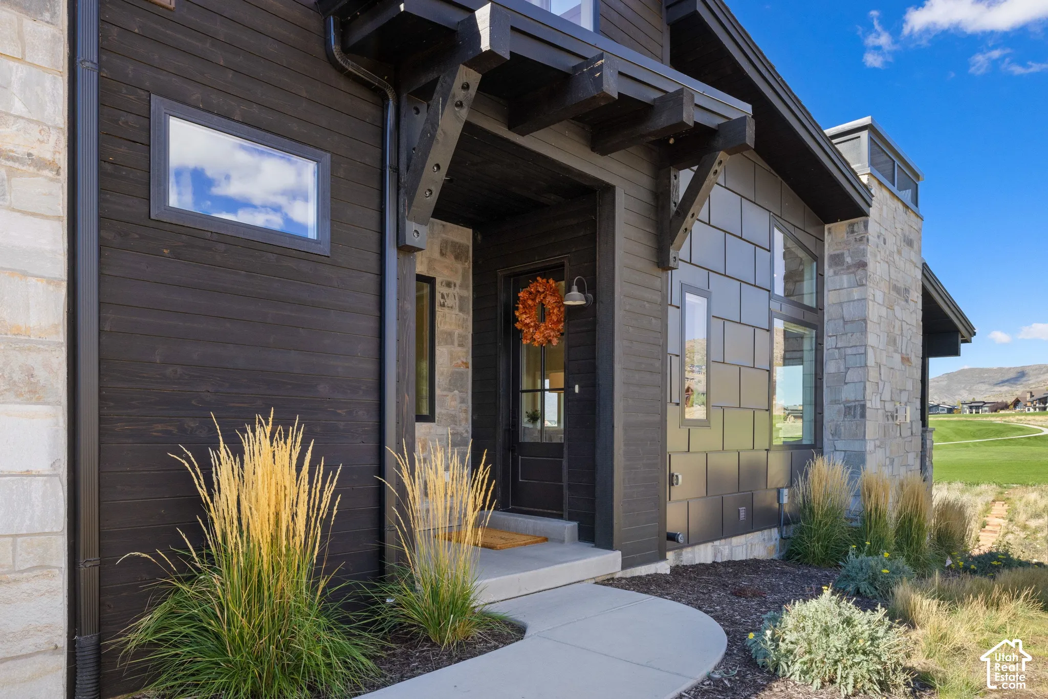 Modern exterior featuring dark horizontal wood siding, metal paneling, stone masonry accents, custom timber corbel detailing, and a glass-paneled entry door