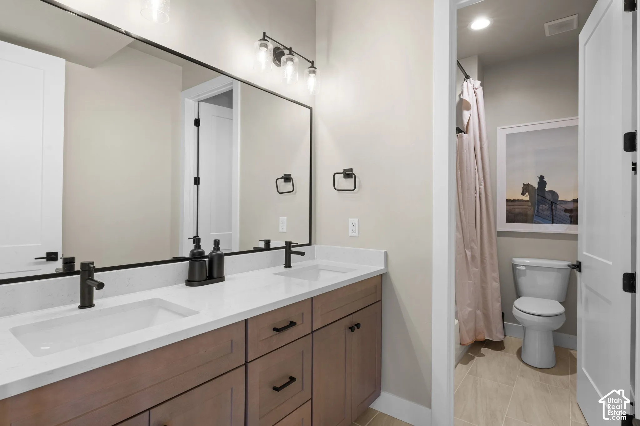 Dual-sink vanity with light-tone stone countertop, wood-finish cabinetry, matte black hardware, and large rectangular mirrors