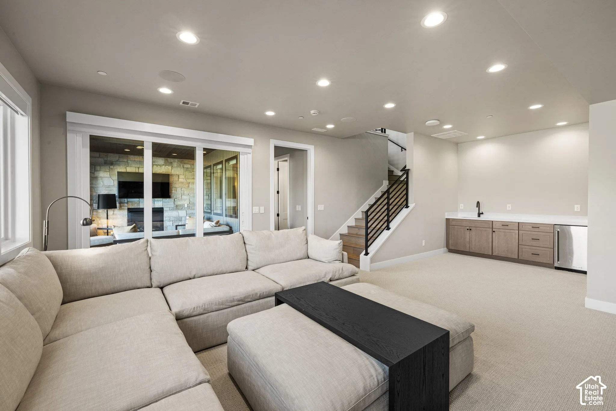 Recessed ceiling lighting, wet bar with cabinetry and sink, and staircase featuring wood treads and a black metal railing