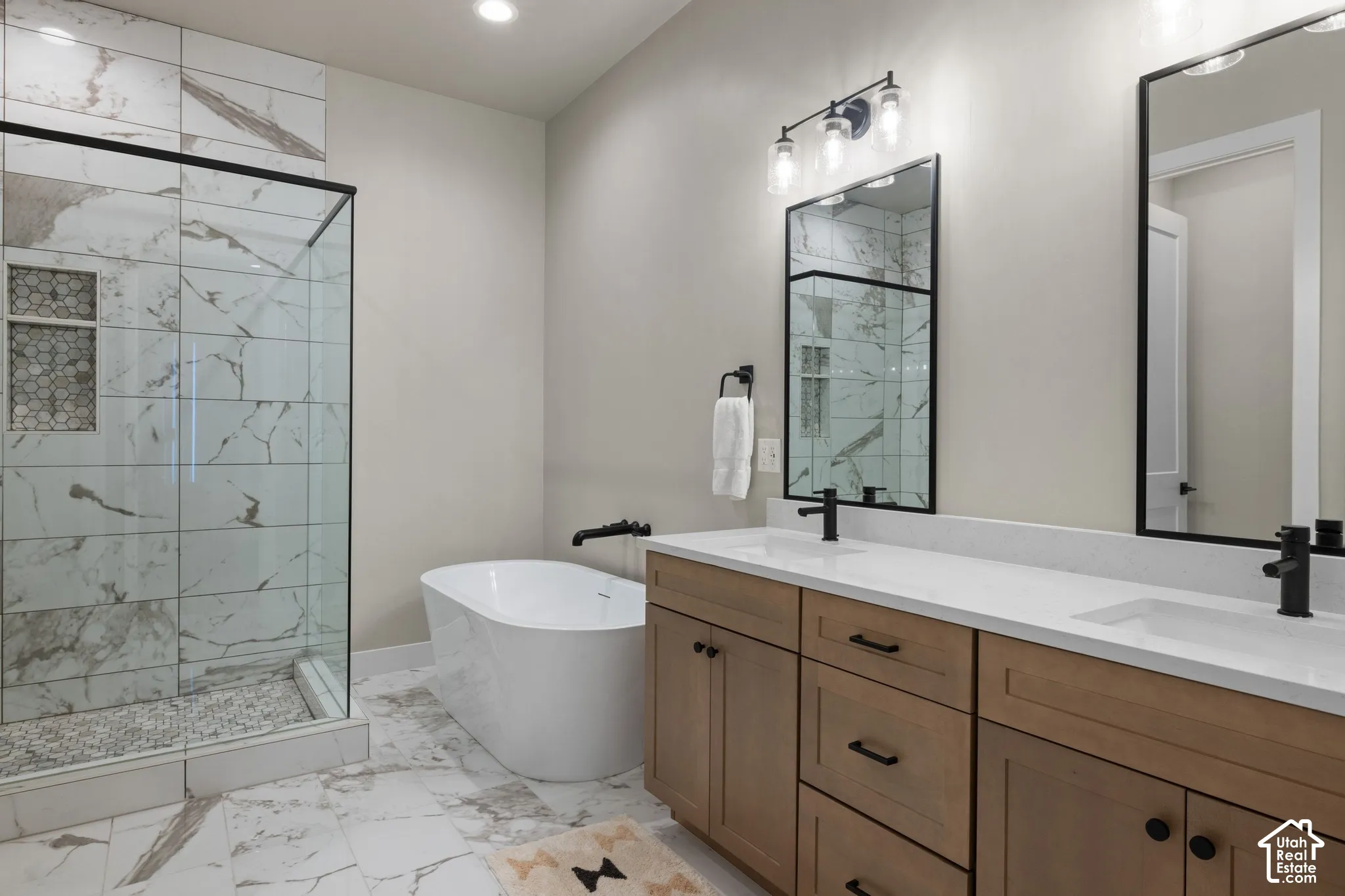 Dual-vanity cabinet with quartz countertop, matte black fixtures, freestanding soaking tub, and glass-enclosed shower with tiled surround