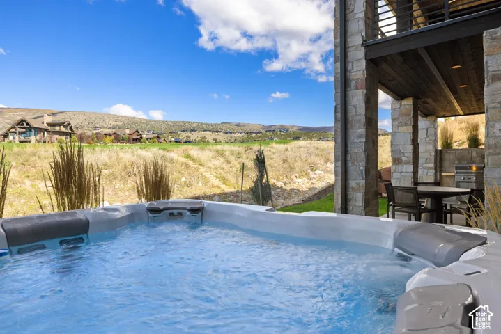 Built-in spa with integrated headrests, stone-clad structural columns, and covered patio featuring a built-in outdoor grill