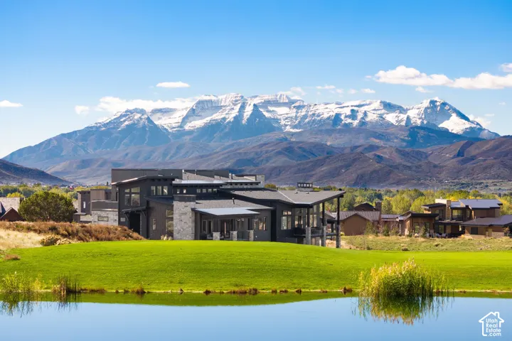Contemporary residence with multi-level rooflines, dark exterior cladding, stone masonry accents, covered outdoor patio, and a backdrop of mountain scenery