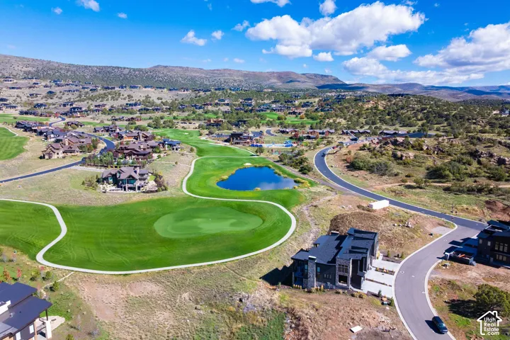 Aerial view showcasing golf course frontage, a natural pond, paved pathways, and mountain terrain
