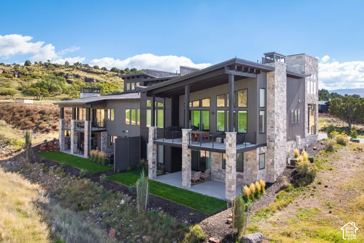 Contemporary multi-level exterior featuring stacked stone masonry, shed rooflines, metal-railed balconies, and a covered ground-level patio