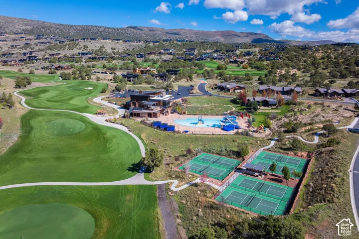 Aerial perspective of a golf course featuring manicured greens, a multi-court tennis complex, an outdoor swimming pool with water slides, and expansive natural mountain terrain