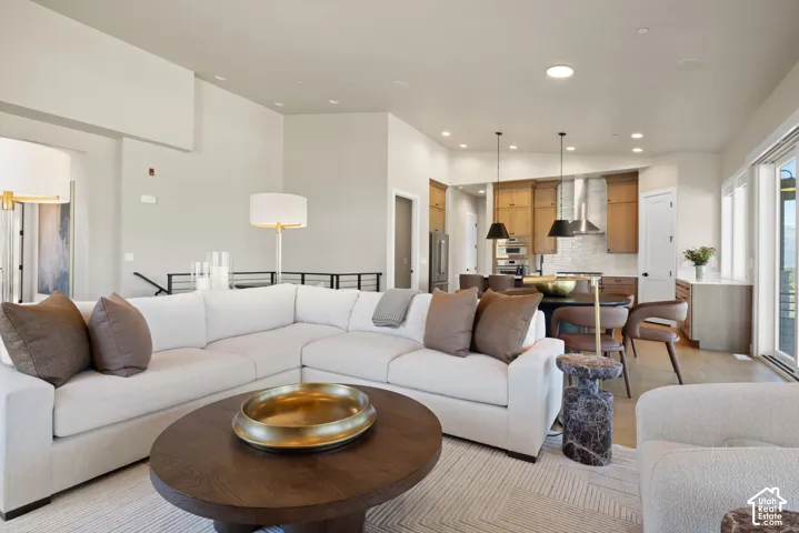 Open-concept living space featuring high ceilings, wood-finish flooring, recessed lighting, and kitchen cabinetry with integrated stainless steel appliances