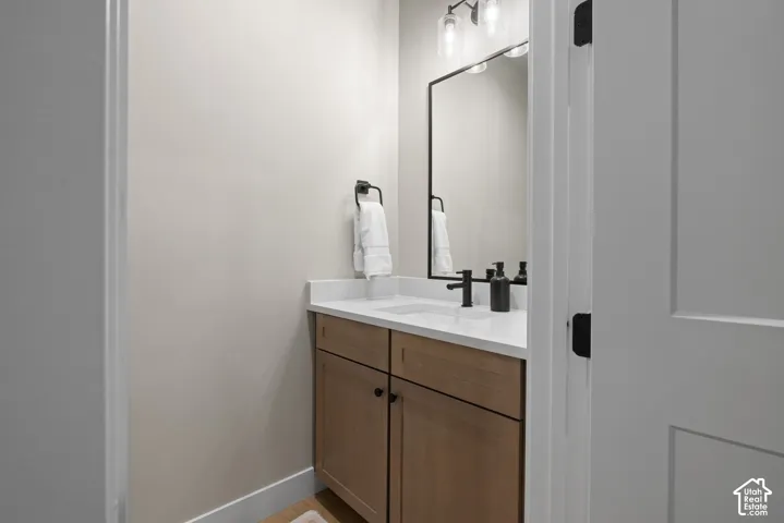 Cabinetry with a light wood finish, white countertop with an integrated rectangular sink, matte black faucet, rectangular wall mirror with a black frame, and three-light glass fixture