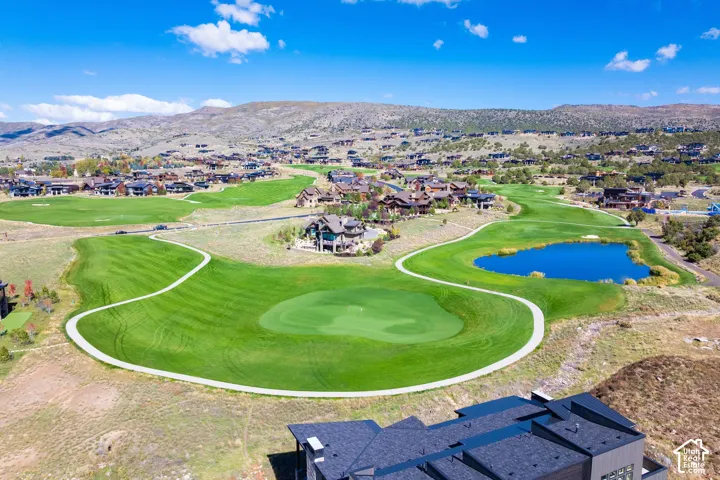 Aerial perspective of a golf course setting featuring manicured fairways, a water feature, paved cart paths, and mountain topography
