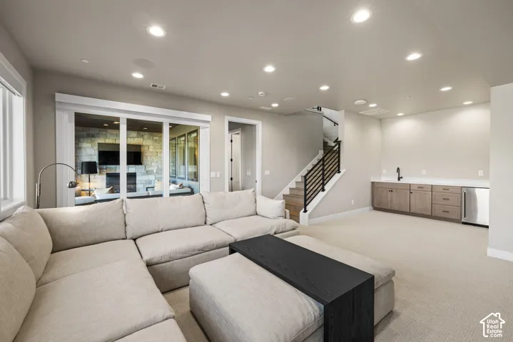 Recessed ceiling lighting, wet bar with cabinetry and sink, and staircase featuring wood treads and a black metal railing