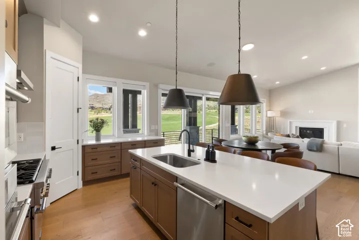 Kitchen featuring a central island with a quartz countertop, stainless steel appliances, wood-finish cabinetry, wood-finish flooring, and pendant lighting