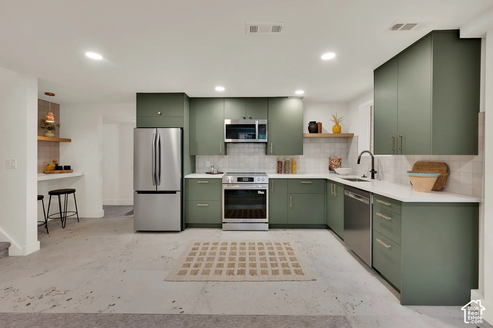 Kitchen featuring matte green cabinetry, stainless steel appliances, white stone countertops, & square-tile backsplash