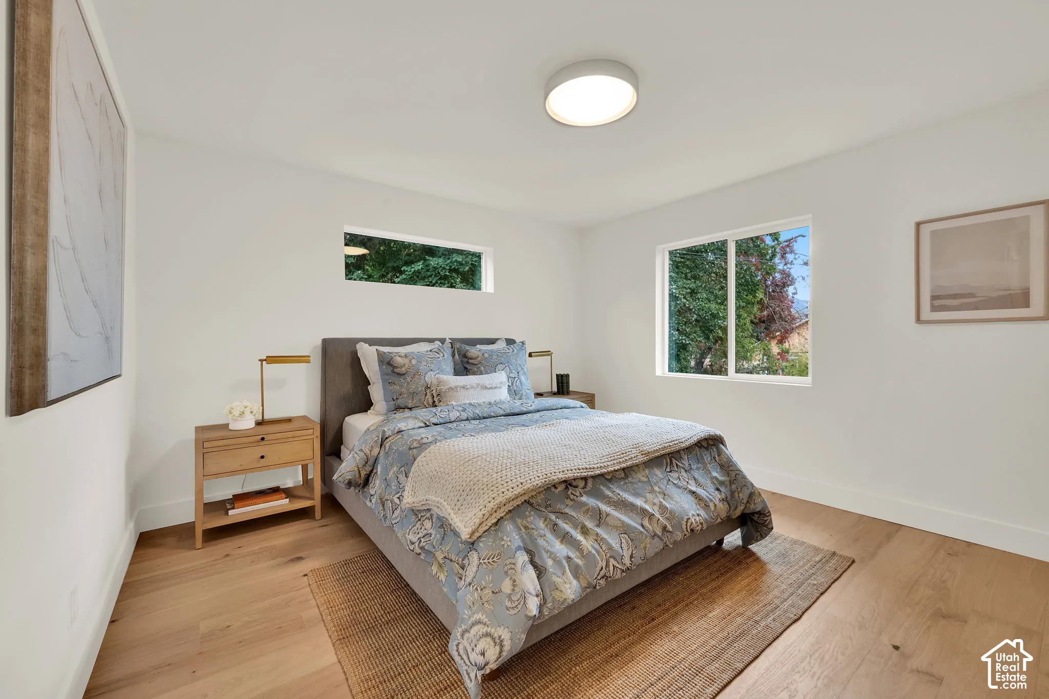 Primary bedroom featuring wood flooring, a sleek circular flush-mount ceiling light, and a wide-format rectangular window
