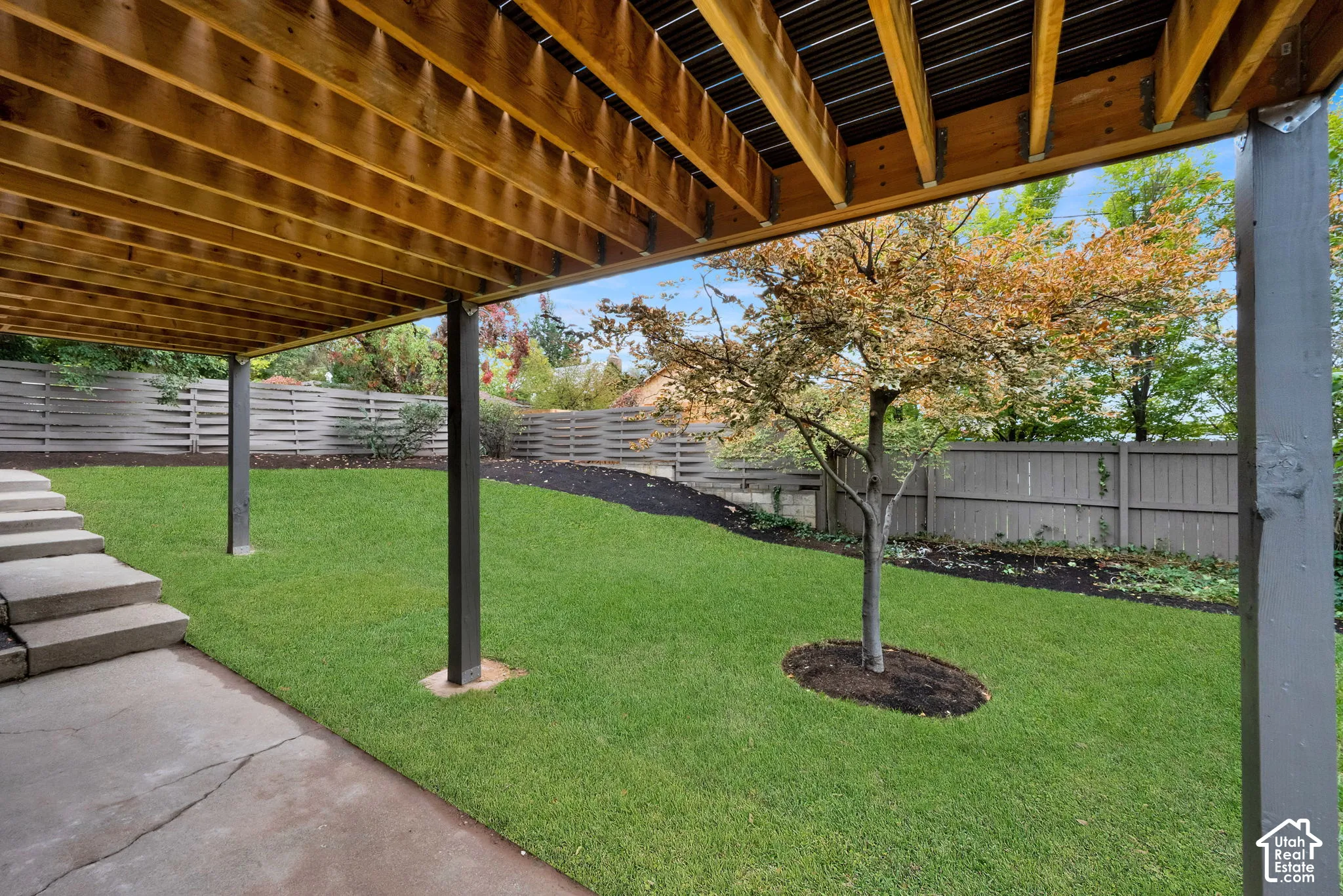 Covered concrete patio featuring tiered concrete steps, a manicured lawn, and perimeter wood fencing