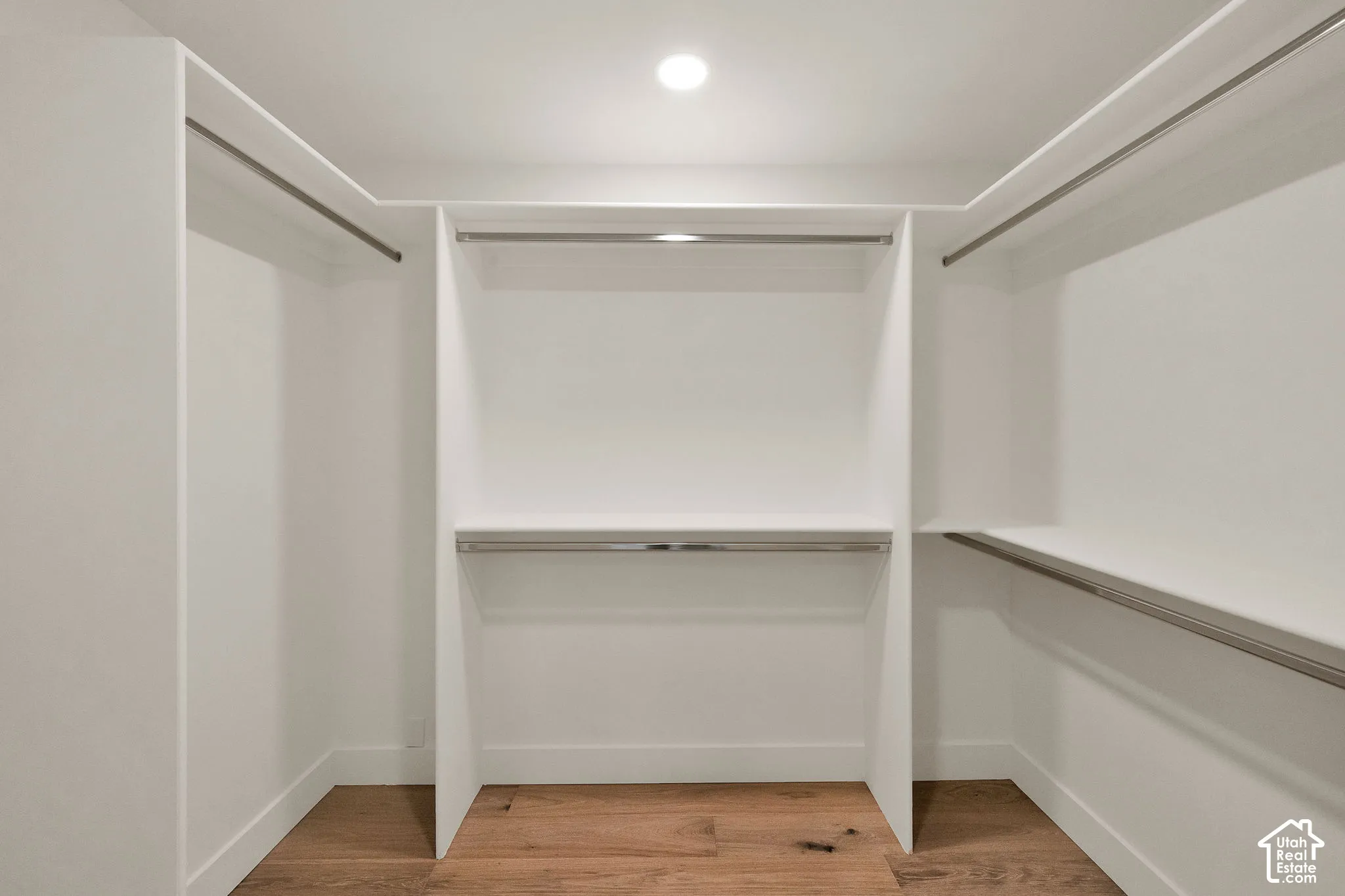Primary walk-in closet featuring white built-in shelving, chrome garment rods, and wood flooring