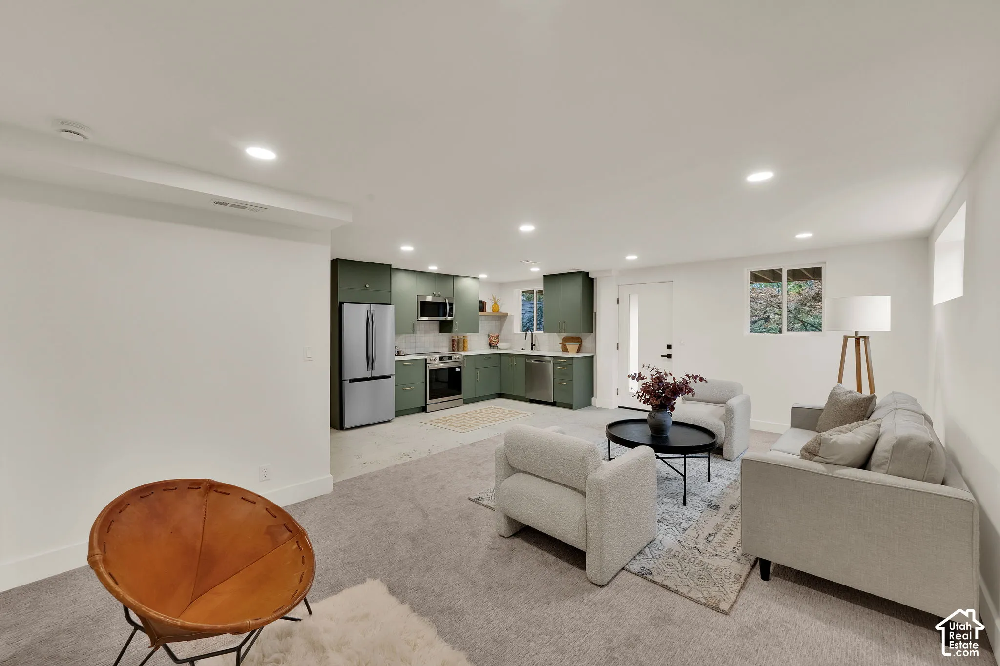 Open-concept layout featuring green cabinetry, stainless steel appliances, quartz countertops, and recessed lighting