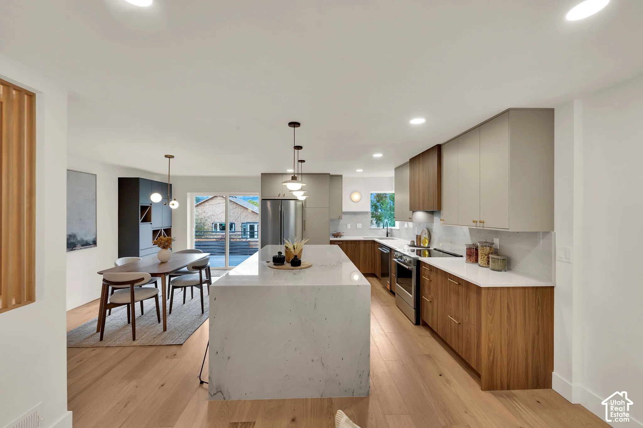 Kitchen featuring a waterfall-edge stone island, two-tone cabinetry with wood-finish base cabinets, light-toned countertop surfaces, stainless steel appliances, and wood flooring