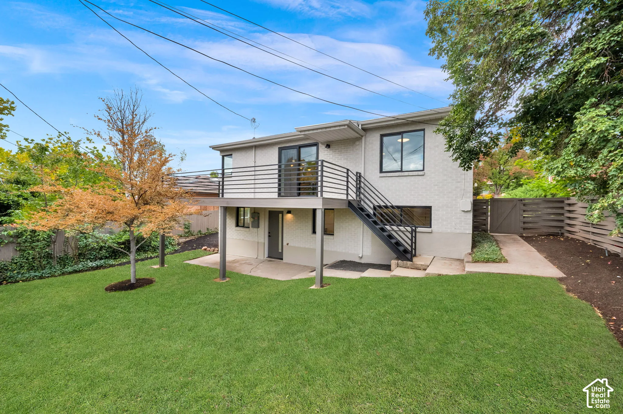 An elevated metal-railing deck, a covered concrete patio, and a fenced backyard with lawn