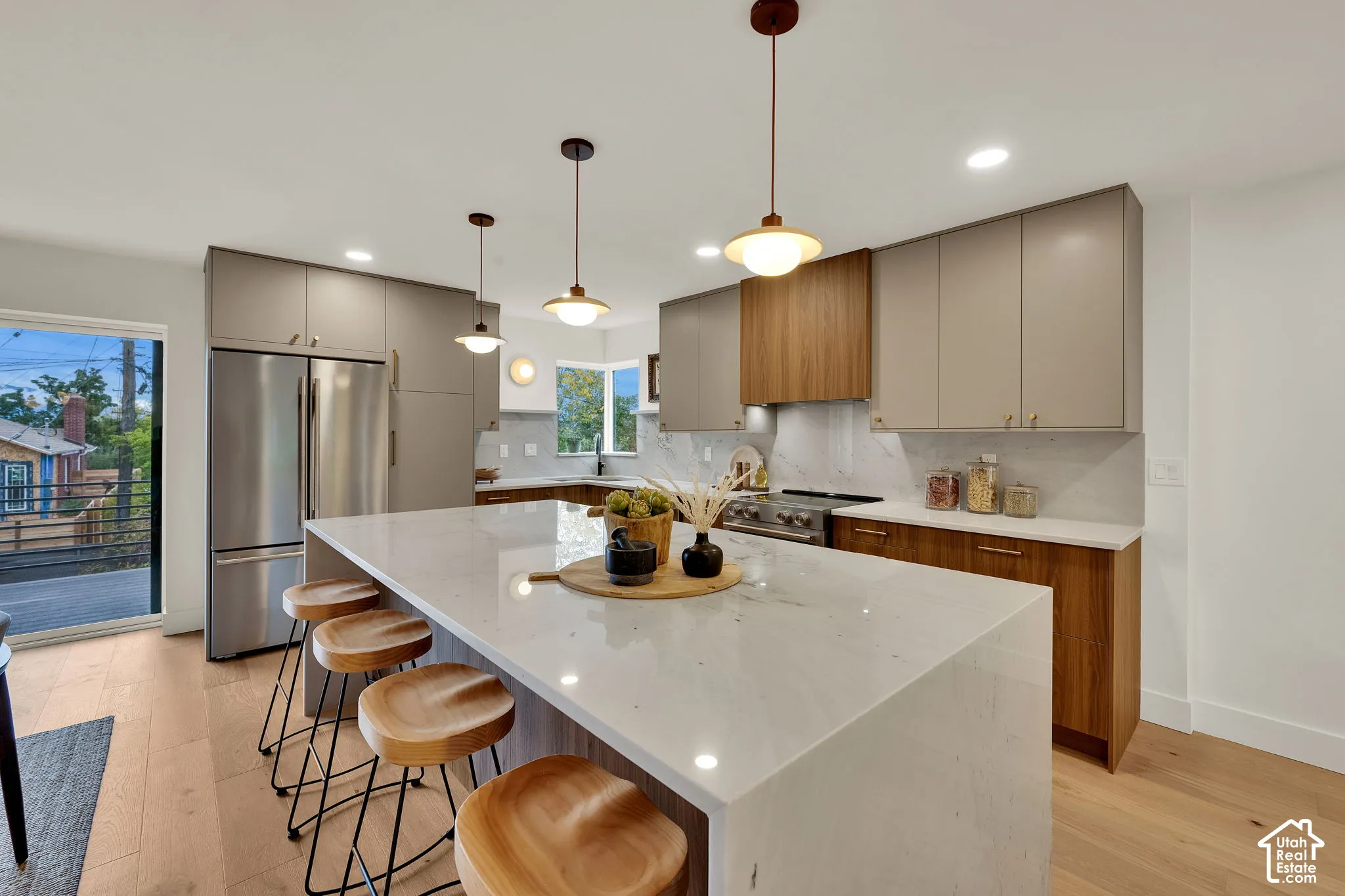 Kitchen featuring two-tone flat-panel cabinetry, a waterfall-edge quartz island, stainless steel appliances, wood flooring, and pendant lighting