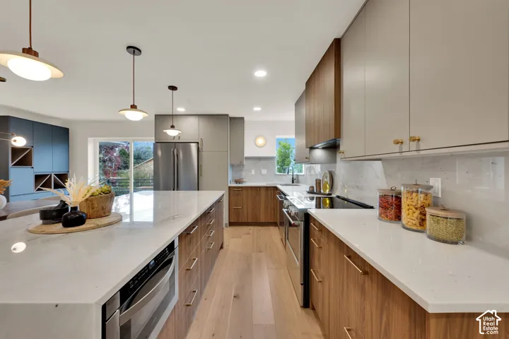 Kitchen featuring wood-finish cabinetry, quartz countertops, stainless steel appliances, wood flooring, and pendant lighting
