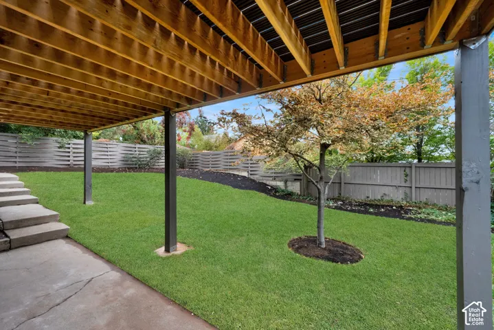Covered concrete patio featuring tiered concrete steps, a manicured lawn, and perimeter wood fencing