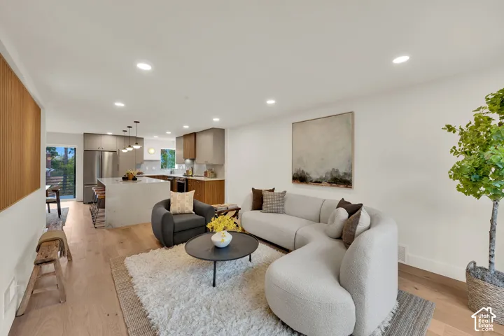 Open-concept kitchen featuring an island with a stone-finish countertop, stainless steel appliances, flat-panel cabinetry, wood flooring, and recessed lighting