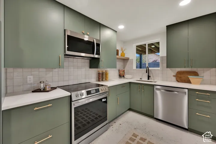 Kitchen featuring matte green cabinetry, brass-finish hardware, stainless steel appliances, & quartz countertops