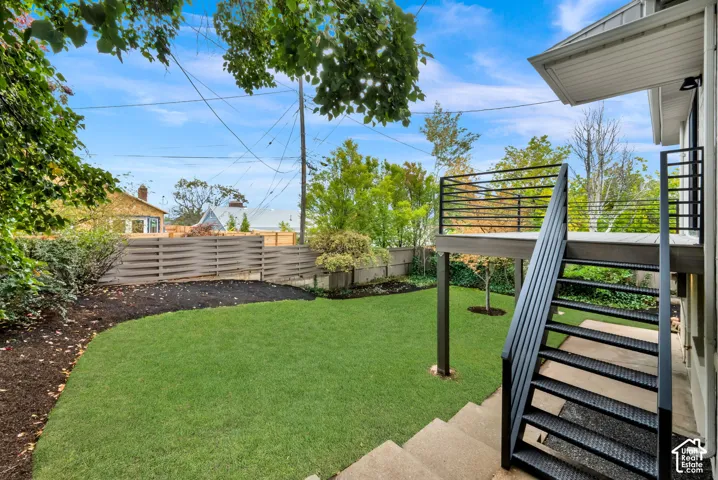 Private backyard featuring a raised composite deck with black metal railing, stairs to the lawn, wood-slat privacy fencing, and mature landscaping