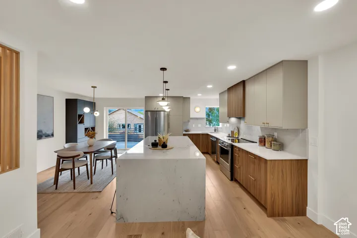 Kitchen featuring a waterfall-edge stone island, two-tone cabinetry with wood-finish base cabinets, light-toned countertop surfaces, stainless steel appliances, and wood flooring