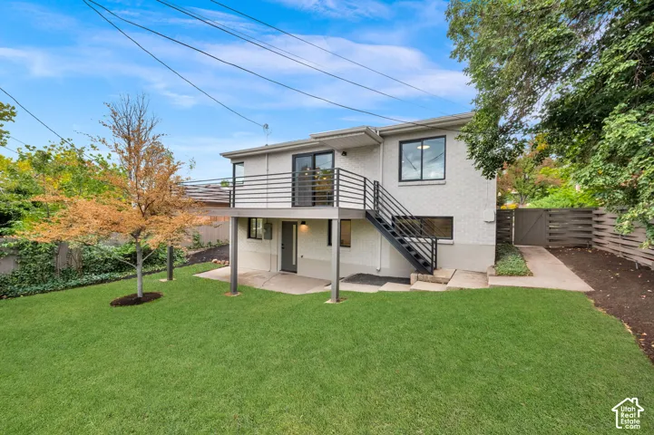 An elevated metal-railing deck, a covered concrete patio, and a fenced backyard with lawn