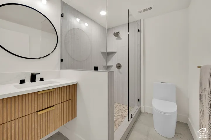 Floating wood-finish vanity with fluted detailing, quartz countertop, walk-in shower with glass enclosure, & decorative pebble flooring