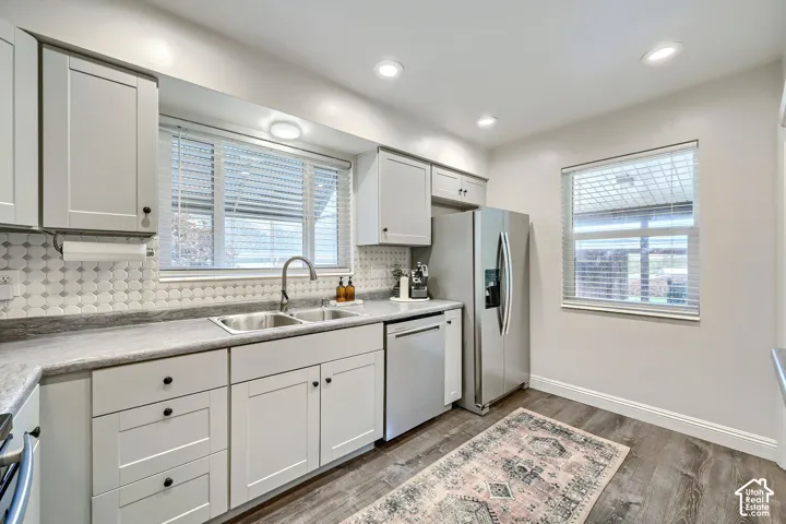 Kitchen featuring light gray shaker-style cabinetry, patterned hexagonal tile backsplash, stainless steel appliances, and wood-finish flooring