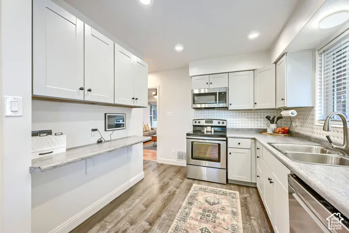 Kitchen featuring shaker-style cabinetry, wood-finish flooring, stainless steel appliances, and stone-finish countertops