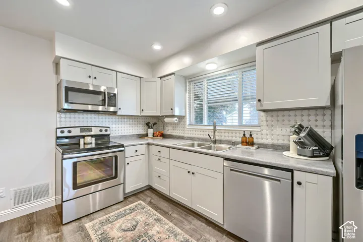 Kitchen featuring shaker-style cabinetry, stainless steel appliances, neutral stone-finish countertops, geometric tile backsplash, and recessed lighting